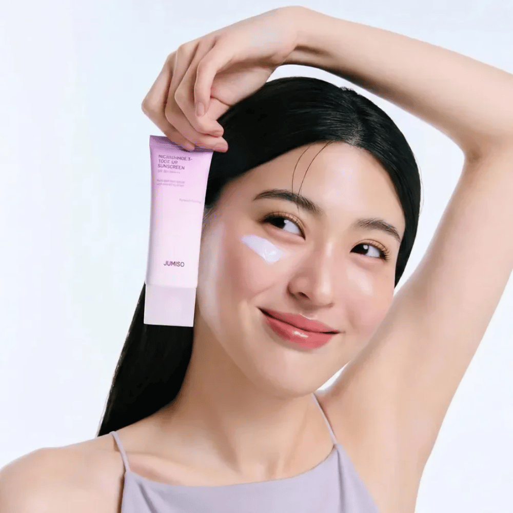 La modella tiene in mano JUMISO Niacinamide 3+ Tone-Up Sunscreen SPF50+ PA++++ – crema solare con niacinamide che uniforma l’incarnato e protegge la pelle.