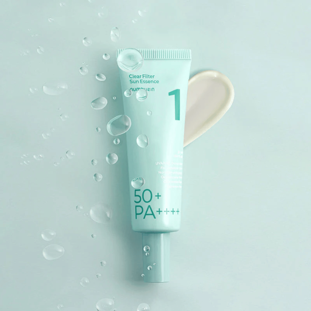 Un tubo azzurro chiaro con No.1 Clear Filter Sun Essence SPF 50+ PA++++. Il tubo è decorato con gocce d'acqua e una goccia del prodotto è mostrata accanto. Il prodotto è progettato per offrire un alto fattore di protezione solare e protezione contro i raggi UVA/UVB.