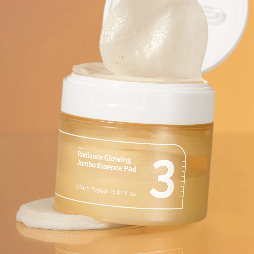 Barattolo aperto con numbuzin No. 3 Radiance Glowing Jumbo Essence Pad, un pad è visibile inclinato contro il bordo, sfondo in tonalità arancione.