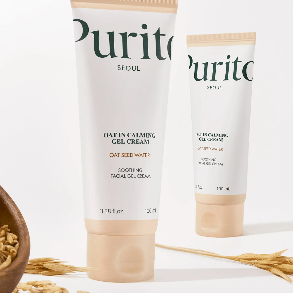 Purito Oat-In Calming Gel Cream in tubetto beige, posizionato con chicchi di avena. Calma la pelle sensibile con acqua d'avena e una leggera texture in gel.