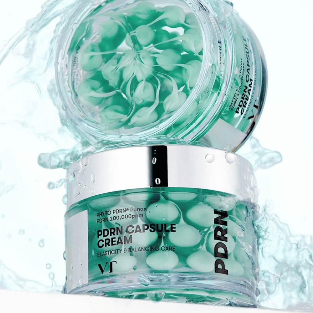 Due barattoli di VT PDRN Capsule Cream impilati con schizzi d'acqua intorno. I barattoli trasparenti mostrano capsule verdi all'interno, con il testo "Elasticity & Balancing Care" visibile sull'etichetta.