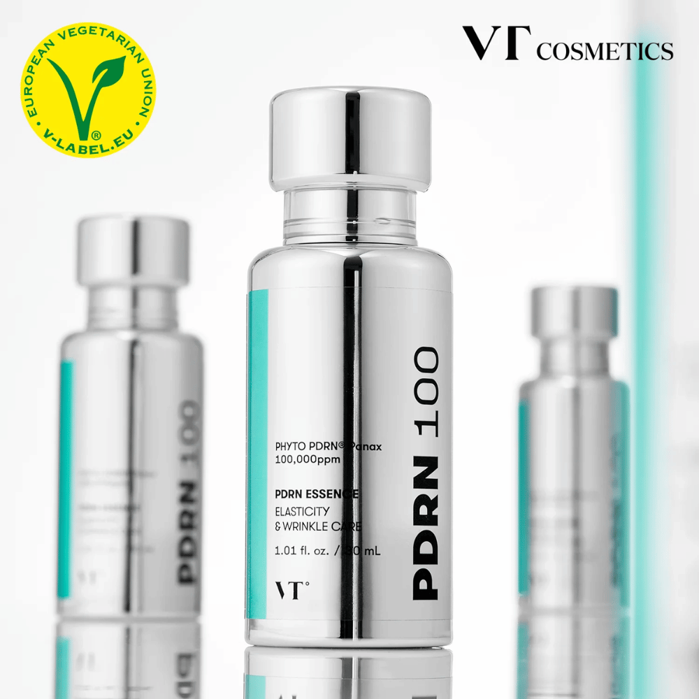 Diverse bottiglie argentate di VT PDRN 100 Essence sono allineate, con chiara etichettatura di 100.000 ppm PDRN e focus su elasticità e cura delle rughe. In alto si vede il logo di VT Cosmetics e un'etichetta V per il contenuto vegetariano.