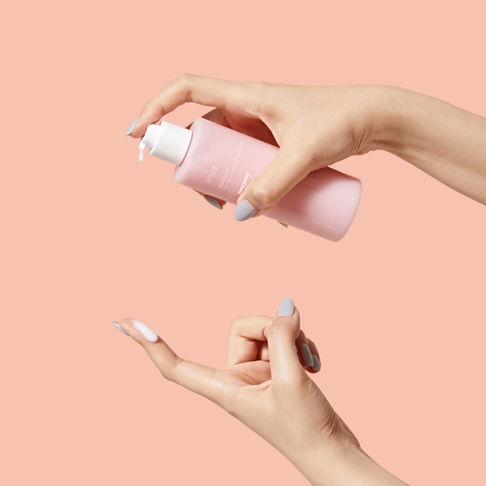 L'immagine mostra le mani di qualcuno che tiene una bottiglia di ANUA Peach 77% Niacin Conditioning Milk. Questo prodotto per la cura della pelle sembra avere una consistenza lattiginosa ed è progettato per nutrire e migliorare la condizione della pelle.