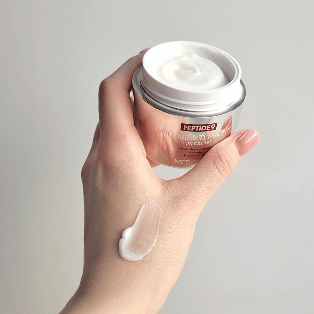 Mano che tiene MEDI-PEEL Peptide 9 Volume & Tension Tox Cream con una dose di crema sul dorso della mano. La formula setosa idrata e dona alla pelle compattezza ed elasticità.