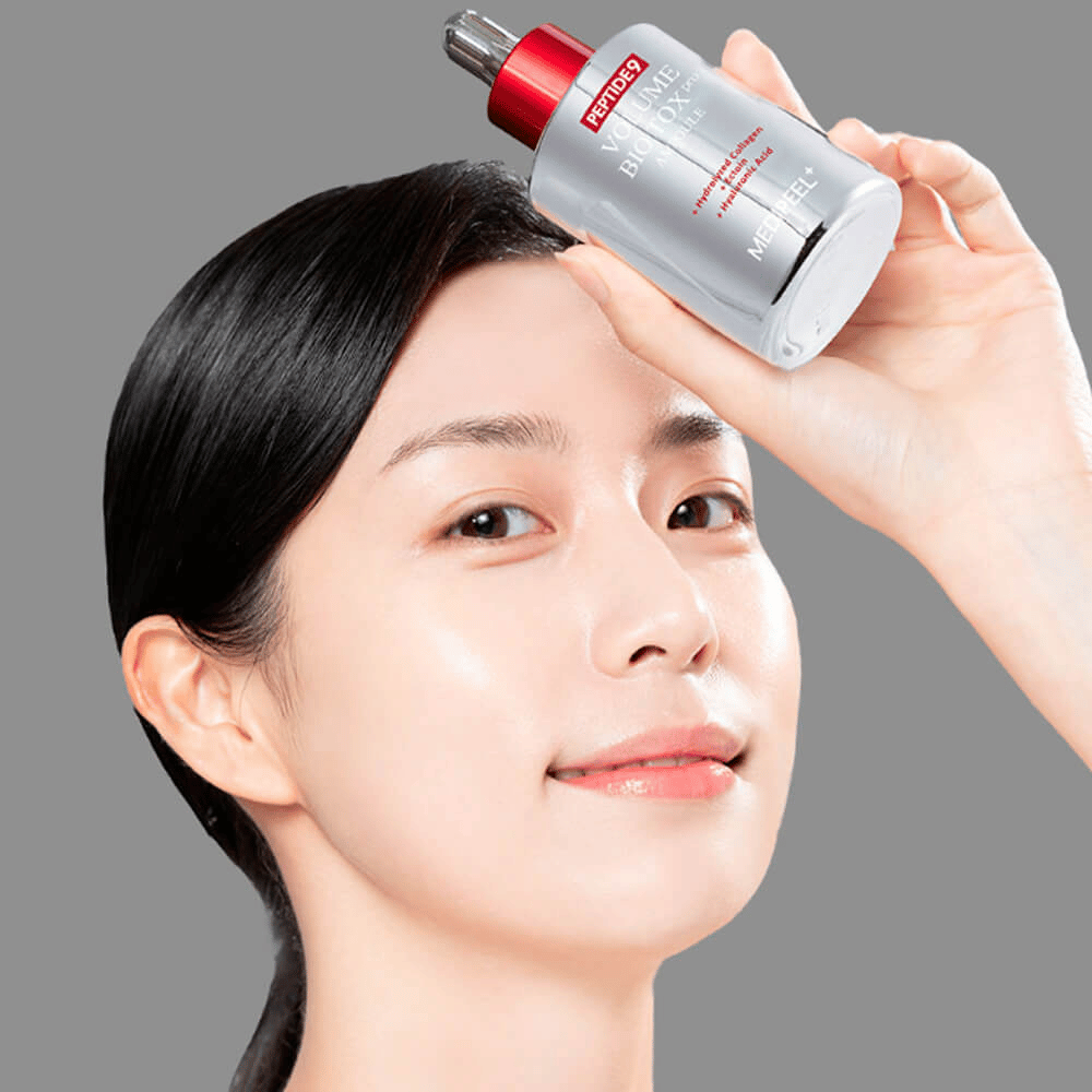 Persona tiene su MEDI-PEEL Peptide 9 Volume Bio Tox Pro Ampoule sulla fronte. La pelle appare idratata e radiosa – il siero rafforza elasticità e compattezza.