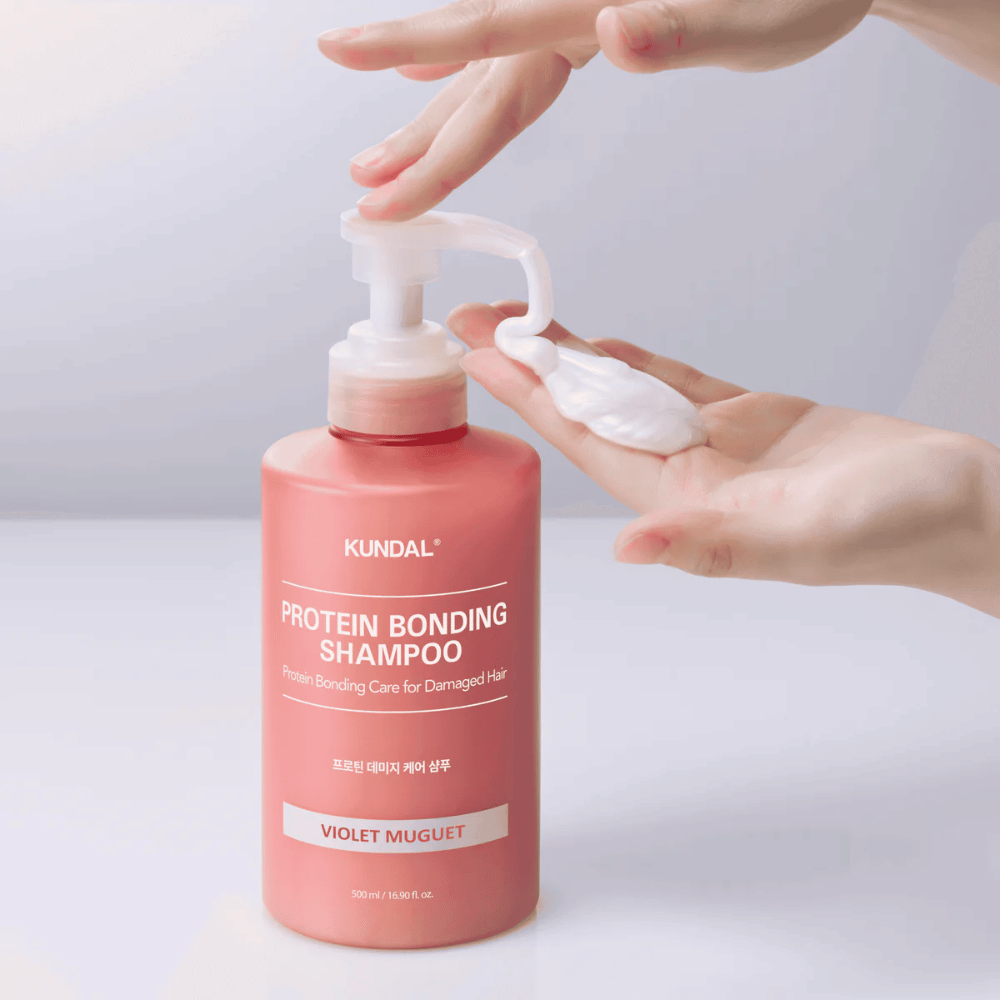 La mano pompa fuori KUNDAL Protein Bonding Shampoo Violet Muguet in consistenza cremosa, shampoo riparatore per capelli danneggiati.