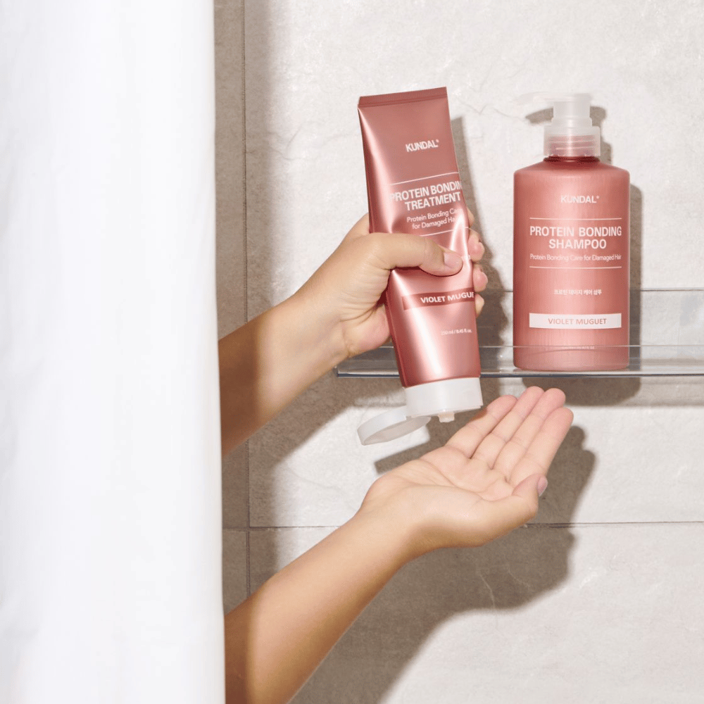 KUNDAL Protein Bonding Treatment Violet Muguet usato nella doccia, con Protein Bonding Shampoo posizionato sullo scaffale accanto.