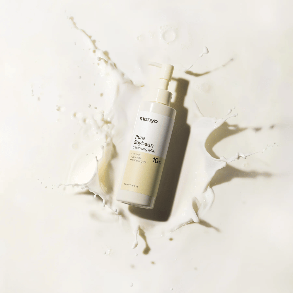 1. Ma:nyo Pure Soybean Cleansing Milk – delicato latte detergente con soia in flacone con pompa circondato da schizzi di latte su sfondo chiaro