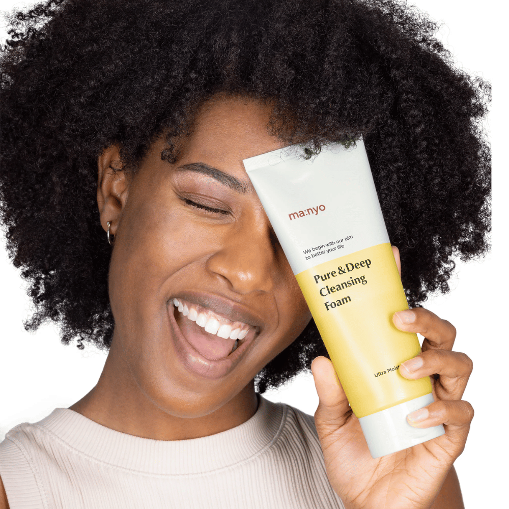 Donna con capelli ricci tiene Ma:nyo Pure & Deep Cleansing Foam – un detergente coreano delicato che rimuove efficacemente sporco e trucco senza seccare la pelle.
