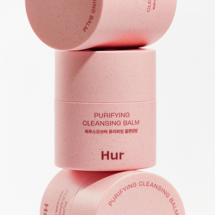 Come Purifying Cleansing Balm in confezione rosa impilata in studio. Balsamo detergente che scioglie efficacemente trucco, sebo e impurità senza seccare la pelle.