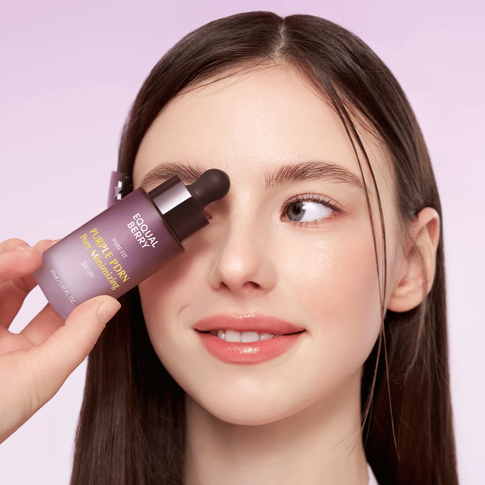 Giovane donna con pelle liscia tiene una bottiglia di Equal Berry Purple PDRN Pore Minimizing Serum contro la fronte, su uno sfondo viola chiaro.