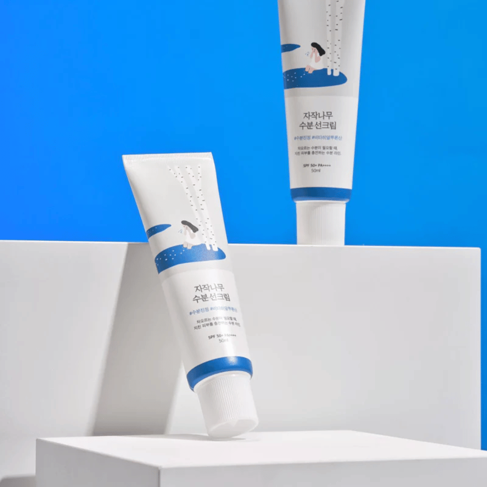 Due tubi con Round Lab Birch Juice Moisturizing Sunscreen SPF50+ PA++++ 50ml che si trovano su uno sfondo blu.