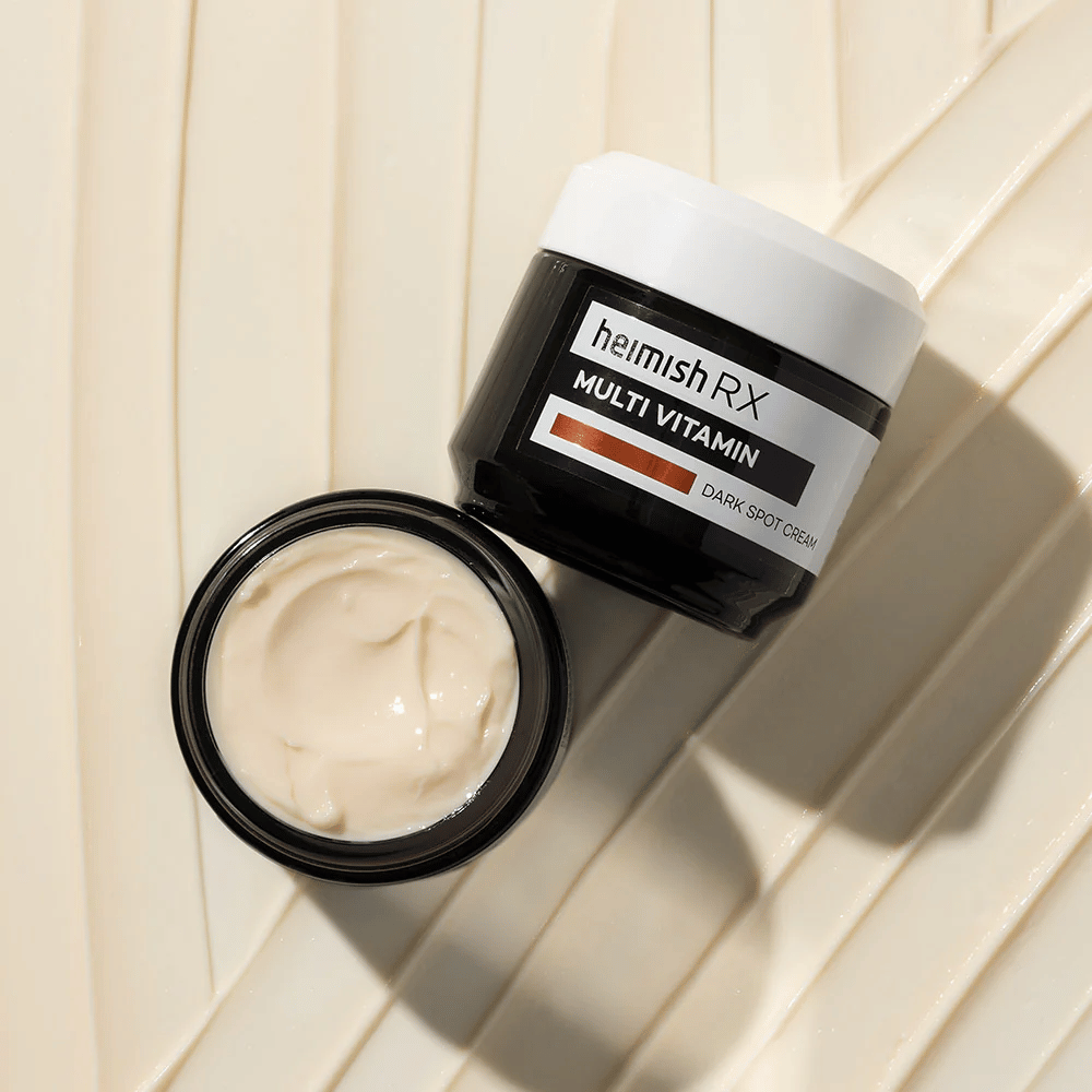 heimish RX Multi Vitamin Dark Spot Cream – una crema viso nutriente per ridurre le macchie scure e dare alla pelle un tono più uniforme. La texture liscia della crema è mostrata in un barattolo aperto con confezione elegante.
