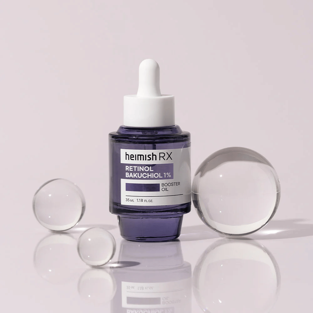 Heimish RX Retinol Bakuchiol Booster Oil 1% in una elegante bottiglia di vetro viola con pipetta. L'olio è posizionato su una superficie riflettente con sfere di vetro intorno, conferendo una sensazione lussuosa e moderna.
