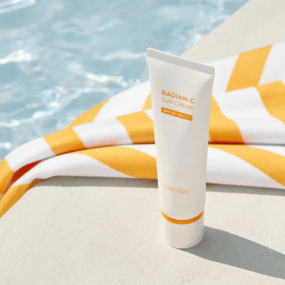 LANEIGE Radian-C Sun Cream si trova accanto a una piscina con un asciugamano a righe gialle e bianche sullo sfondo.
