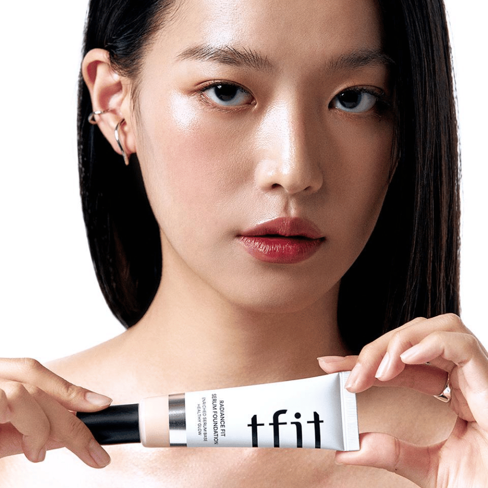 Modello con pelle liscia e lucente tiene in mano TFIT Radiance Fit Serum Foundation, che esalta la finitura naturale e la luminosità del prodotto.