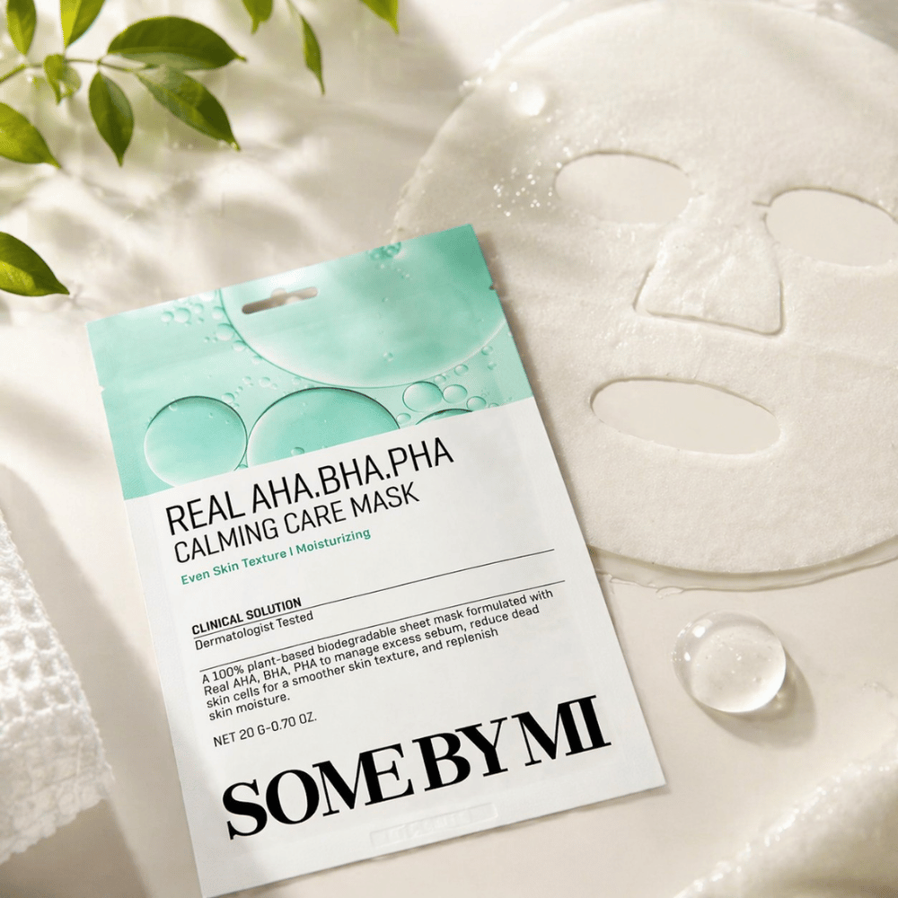 SOME BY MI Real AHA.BHA.PHA Calming Care Mask è mostrata insieme alla maschera in tessuto aperta. Intorno al prodotto si vedono gocce di idratazione e foglie verdi che rafforzano la sensazione di idratazione, cura lenitiva ed esfoliazione delicata. L'immagine mette in risalto l'attenzione della maschera verso una texture della pelle più uniforme e un migliore equilibrio di idratazione.