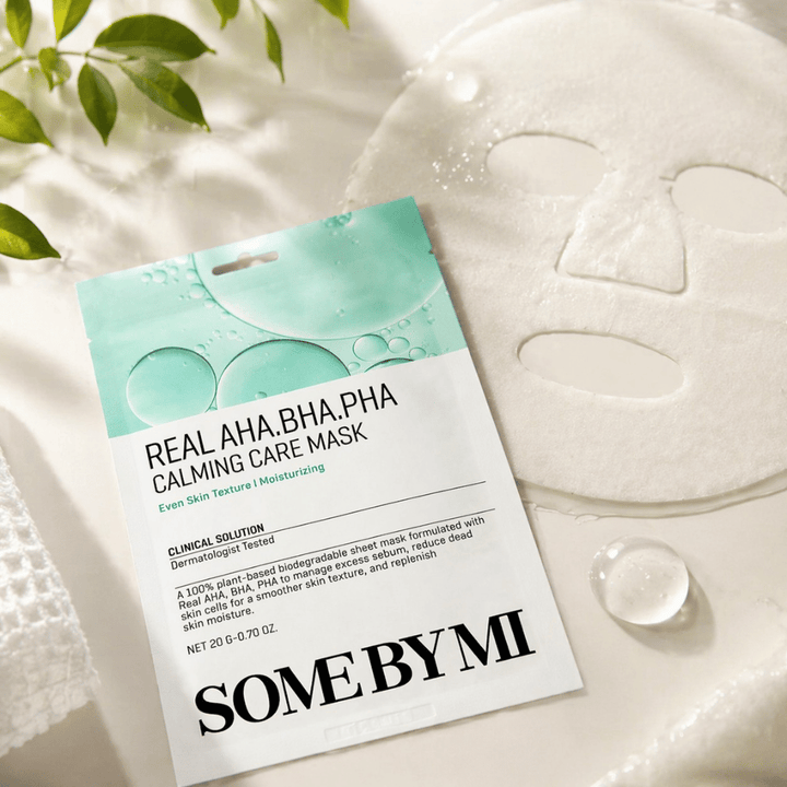 SOME BY MI Real AHA.BHA.PHA Calming Care Mask è mostrata insieme alla maschera in tessuto aperta. Intorno al prodotto si vedono gocce di idratazione e foglie verdi che rafforzano la sensazione di idratazione, cura lenitiva ed esfoliazione delicata. L'immagine mette in risalto l'attenzione della maschera verso una texture della pelle più uniforme e un migliore equilibrio di idratazione.