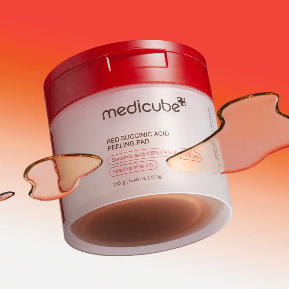 Medicube Red Succinic Acid Peeling Pad in un barattolo bianco e rosso, posizionato su uno sfondo sfumato in rosso e arancione. Il prodotto contiene acido succinico e niacinamide per esfoliazione e miglioramento della pelle. La texture liquida è visibile attorno al barattolo.
