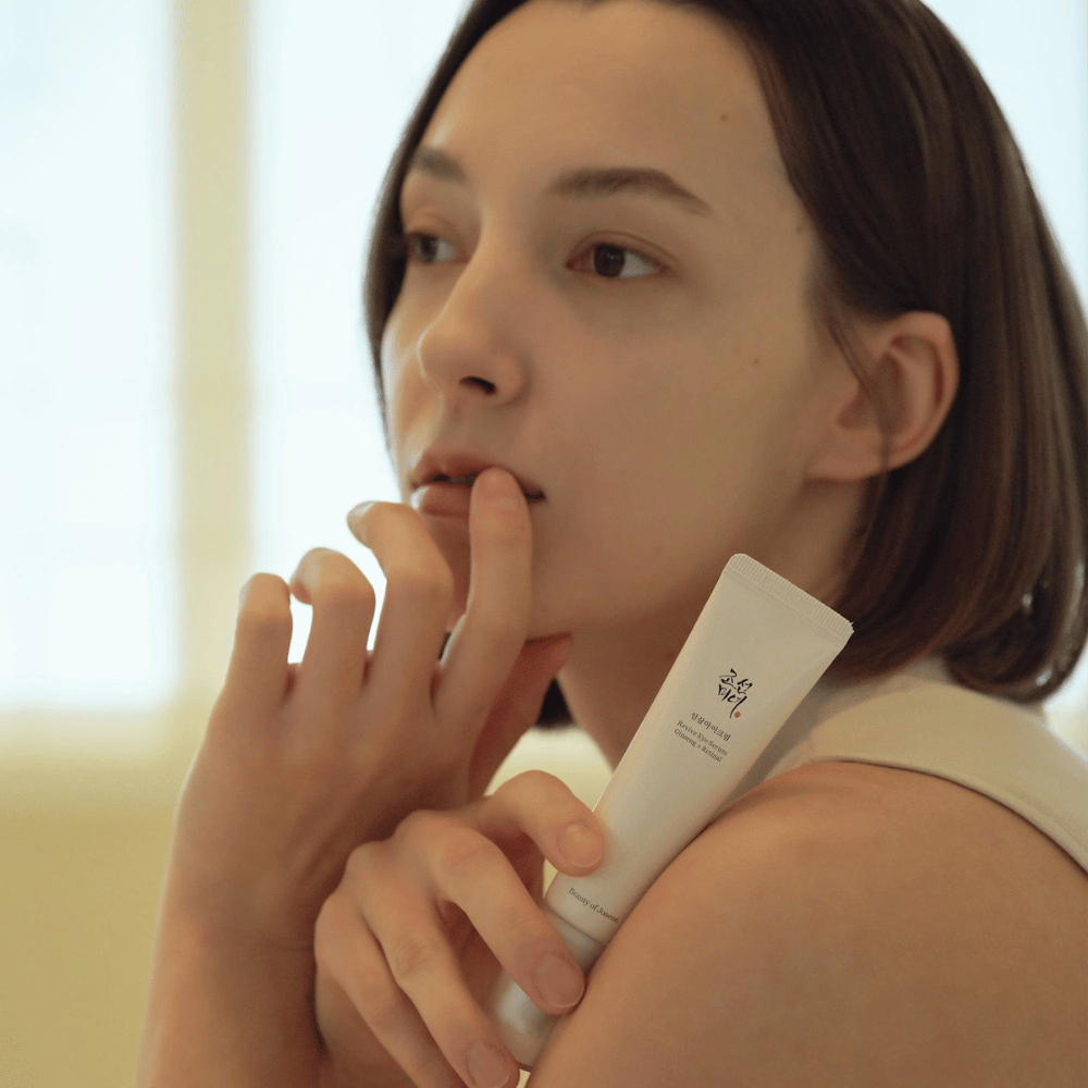 Modello tiene in mano Beauty of Joseon Revive Eye Serum e applica delicatamente sulla pelle per un contorno occhi idratato e liscio.