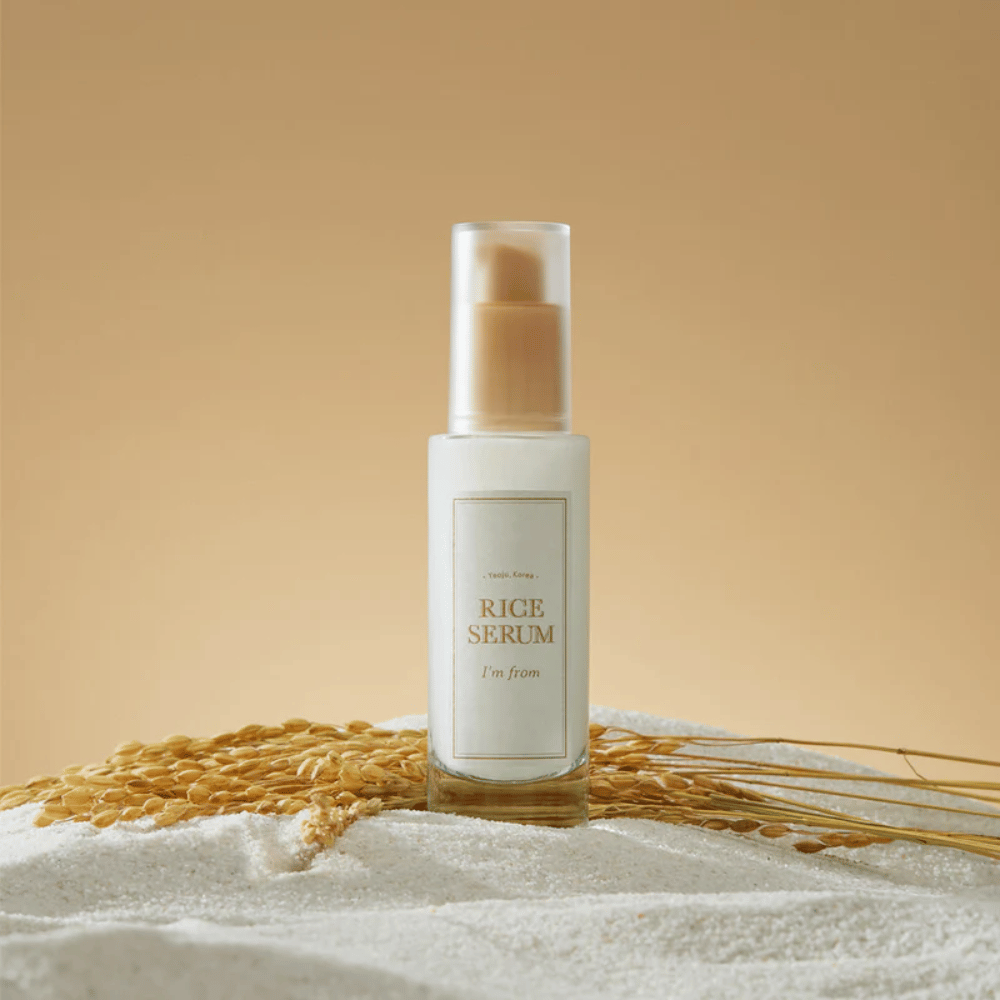 Bottiglia con "I'm from" Rice Serum, circondata da chicchi di riso e spighe di riso su uno sfondo caldo.