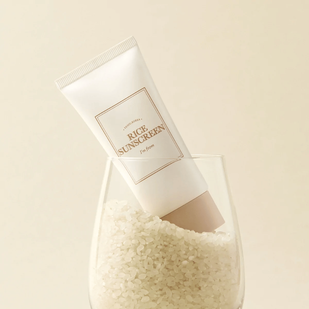 Tubo con "I'm from" Rice Sunscreen, SPF50+ PA++++, posizionato in un bicchiere con chicchi di riso.