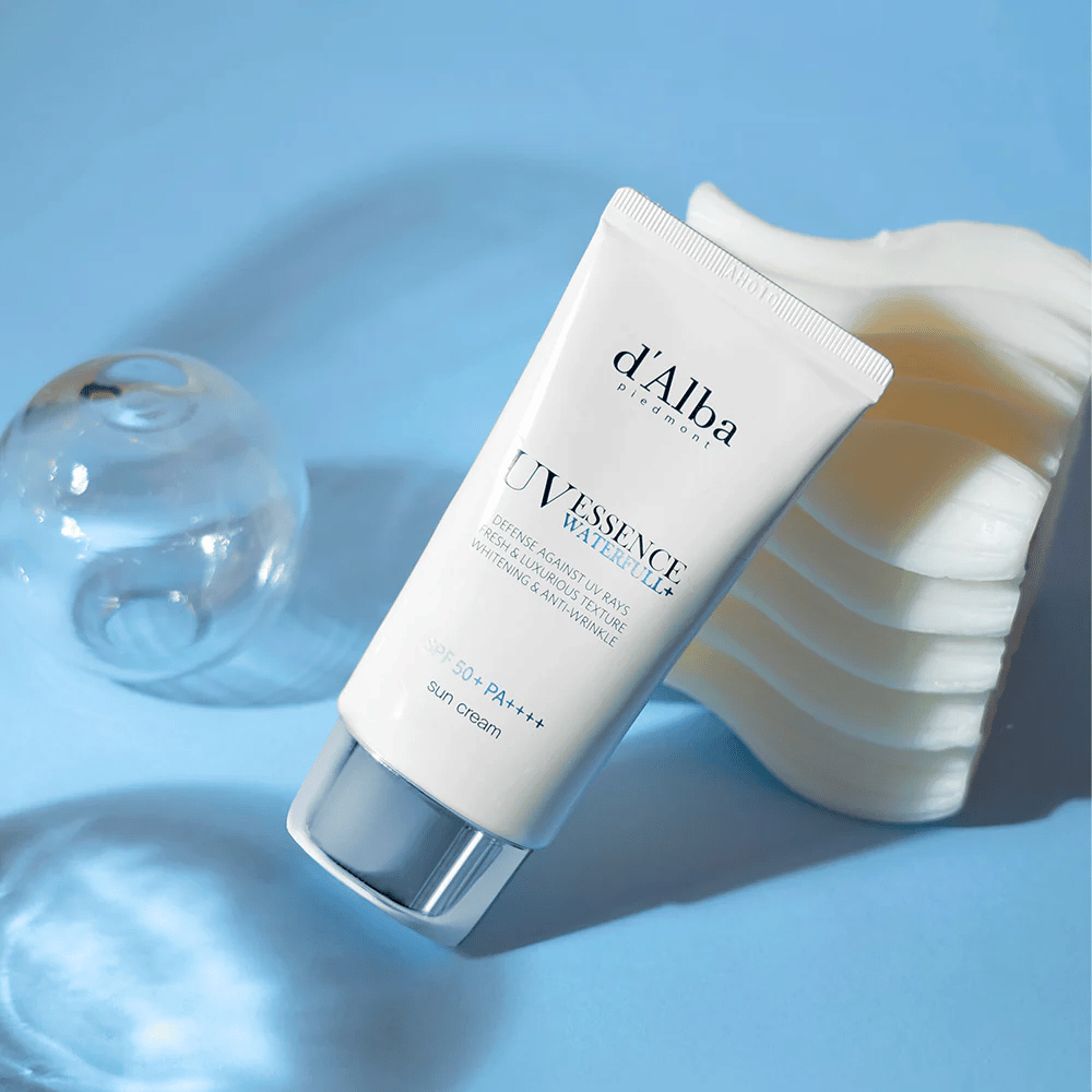 d'Alba UV Essence Waterfull+ Sun Cream con SPF 50+ PA++++ giace su uno sfondo blu con riflessi di luce ed elementi decorativi – evidenziando le proprietà fresche e idratanti della crema solare.