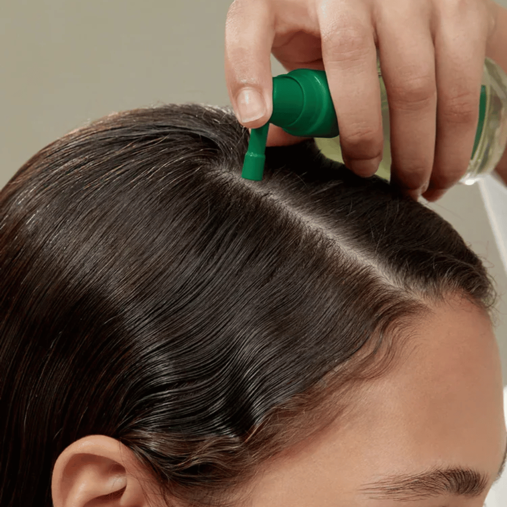 Una persona applica AROMATICA Rosemary Root Enhancer direttamente sul cuoio capelluto con l’aiuto del beccuccio mirato. L’immagine mostra come il prodotto viene utilizzato per la cura del cuoio capelluto e il rafforzamento delle radici dei capelli.