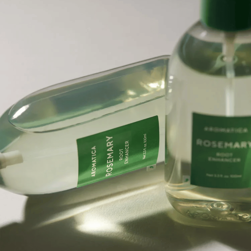 Due flaconi di AROMATICA Rosemary Root Enhancer con cappuccio protettivo trasparente ed etichetta verde. Primo piano che mette in risalto il design premium del prodotto e il concetto di cura naturale dei capelli.
