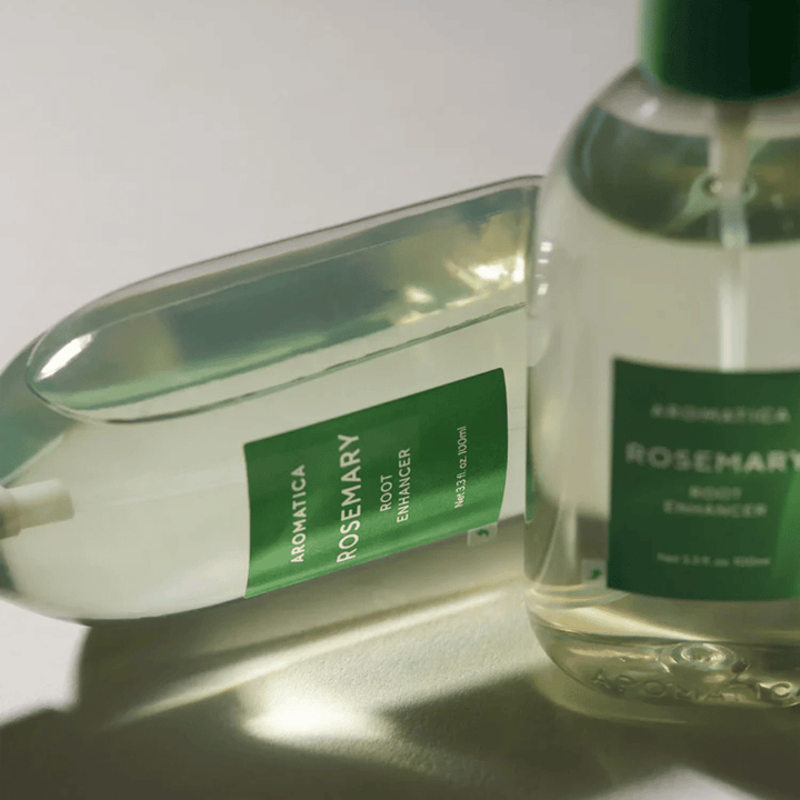 Due flaconi di AROMATICA Rosemary Root Enhancer con cappuccio protettivo trasparente ed etichetta verde. Primo piano che mette in risalto il design premium del prodotto e il concetto di cura naturale dei capelli.