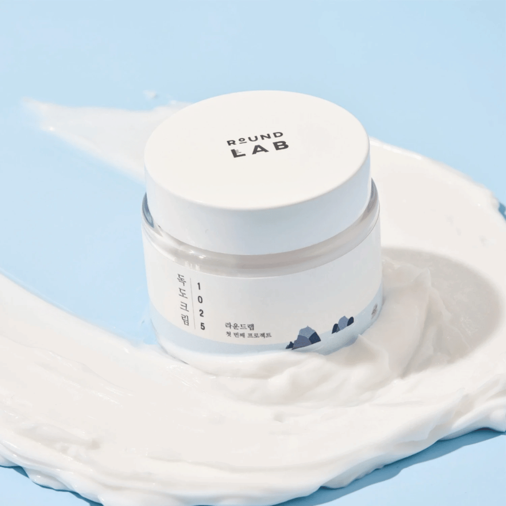 Un barattolo con Round Labs 1025 Dokdo Cream 80 ml che fornisce idratazione, posizionato su uno sfondo blu vivace.