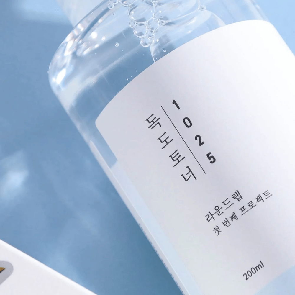 Primo piano di una bottiglia trasparente Round Lab 1025 Dokdo Toner, riempita con liquido chiaro, su sfondo blu.
