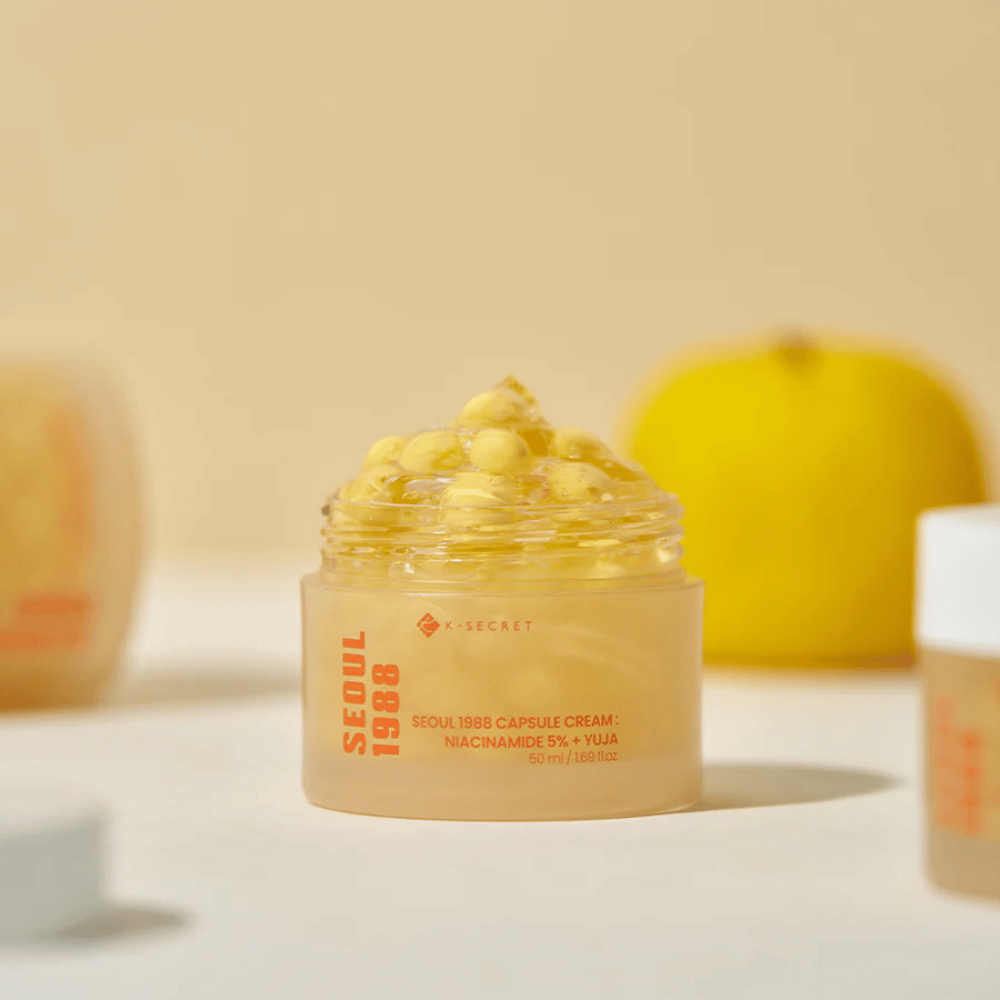 Barattolo aperto con capsule gialle accanto a un frutto di yuja tagliato a metà che evidenzia la formula ricca di vitamina C.