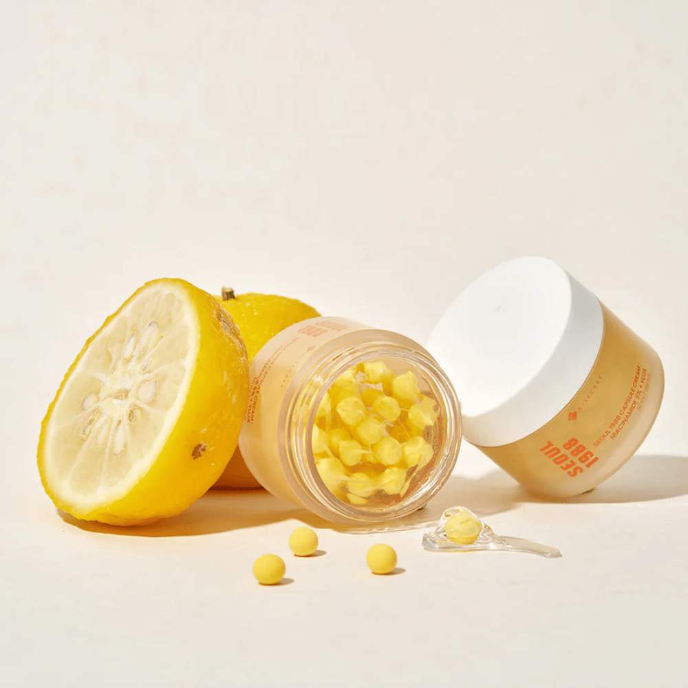 Barattolo aperto con capsule gialle accanto a un frutto di yuja tagliato a metà che evidenzia la formula ricca di vitamina C.