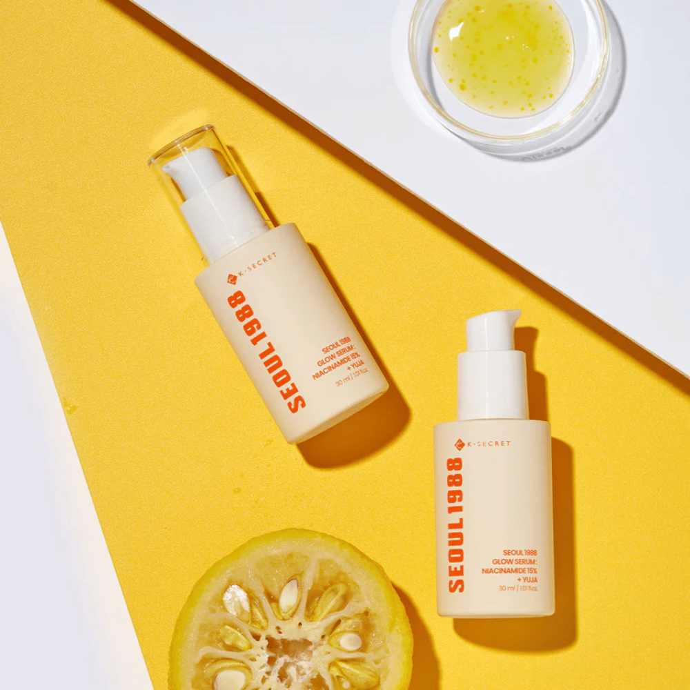 Due bottiglie di Seoul 1988 Glow Serum posizionate su sfondo giallo insieme a una ciotola con siero giallo e un agrume tagliato a metà.