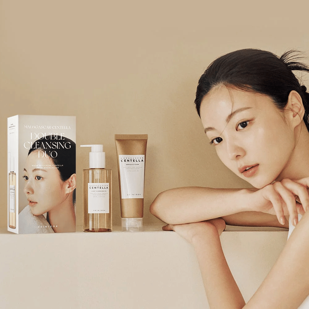 SKIN1004 Madagascar Centella Double Cleansing Duo Set con scatola, detergente oleoso, schiuma detergente e modello con pelle idratata su sfondo beige.