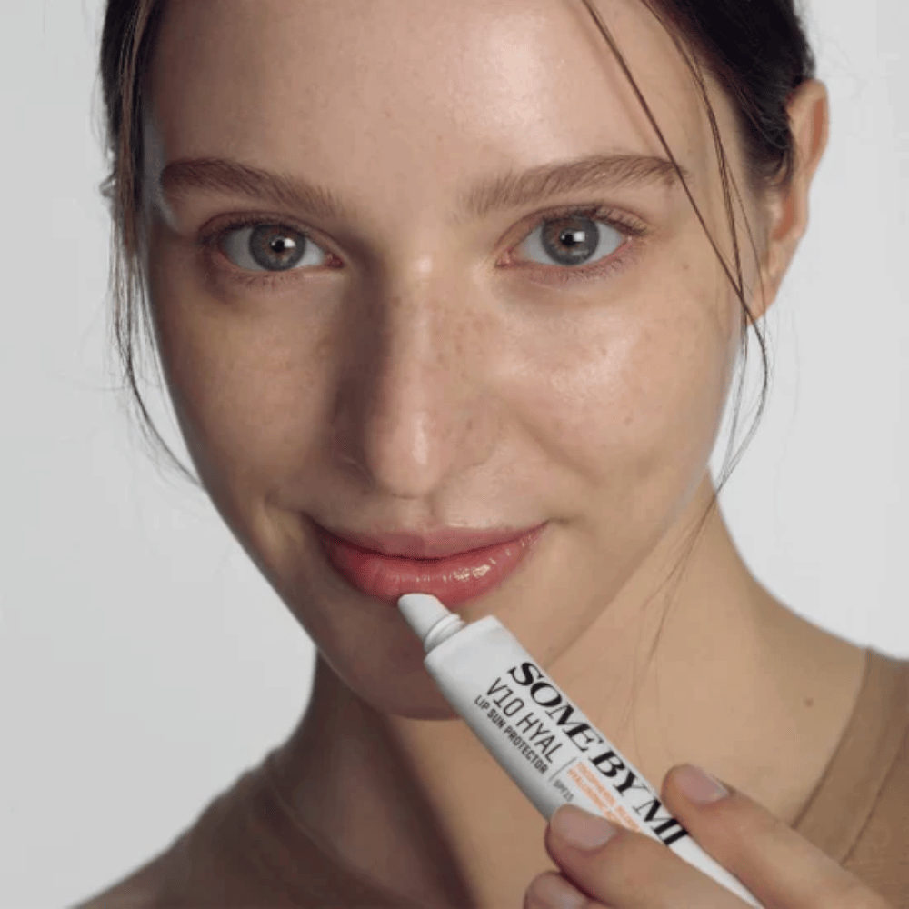 Una donna tiene in mano un tubo V10 Hyal Lip Sun Protector SPF15 7ml balsamo labbra per la protezione solare e l'idratazione, di SOME BY MI.