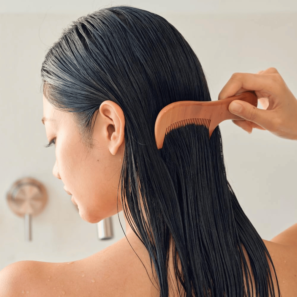 Una persona pettina i capelli lunghi e bagnati con un pettine a denti larghi dopo l’applicazione di Heveblue Salmon Pullkeratin Centella Hair Treatment. Illustra l’effetto districante ed emolliente per un risultato più liscio.