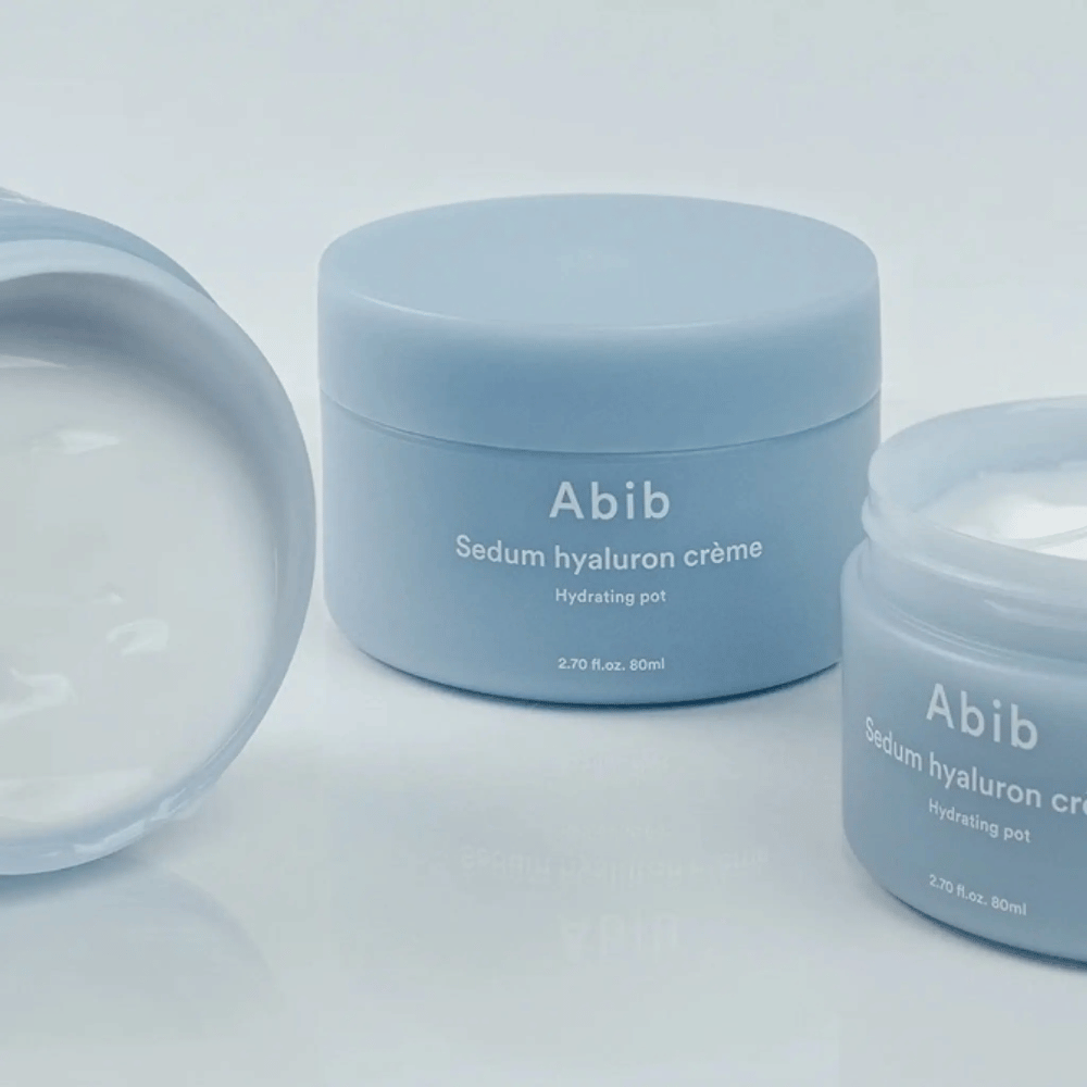 Tre barattoli di Abib Sedum Hyaluron Crème Hydrating Pot 80 ml in un design minimalista azzurro chiaro, uno dei quali mostra l'interno cremoso bianco.