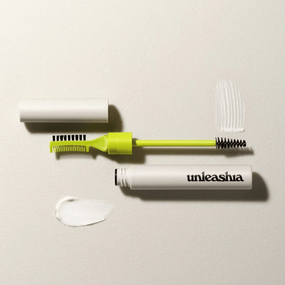 Un set per scolpire le sopracciglia con un pettine verde, una spazzola nera e un tubetto bianco etichettato "unleashia" su uno sfondo chiaro con un grumo di prodotto trasparente.