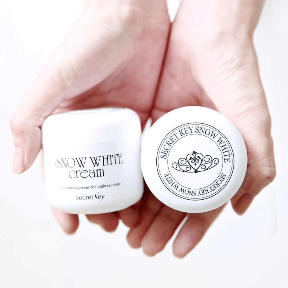 Due barattoli Secret Key Snow White Cream tenuti nelle mani, uno mostra il coperchio e uno mostra la parte anteriore.