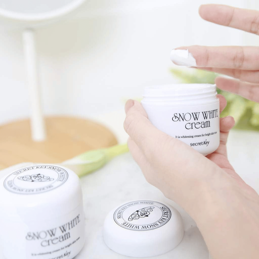 Mano che prende crema bianca da un barattolo Secret Key Snow White Cream su un tavolo da trucco.