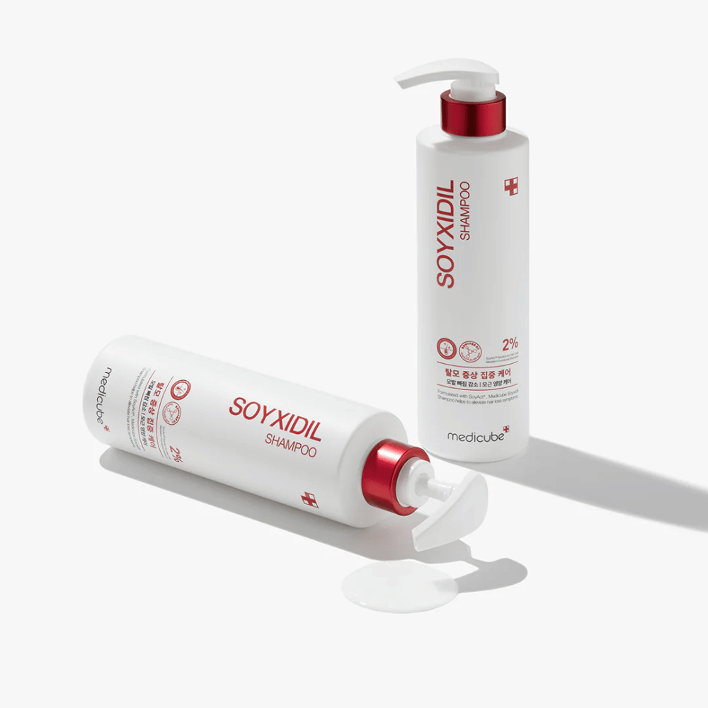 Due bottiglie di Medicube Soyxidil Shampoo in design bianco e rosso, una in piedi e una sdraiata con shampoo versato accanto.