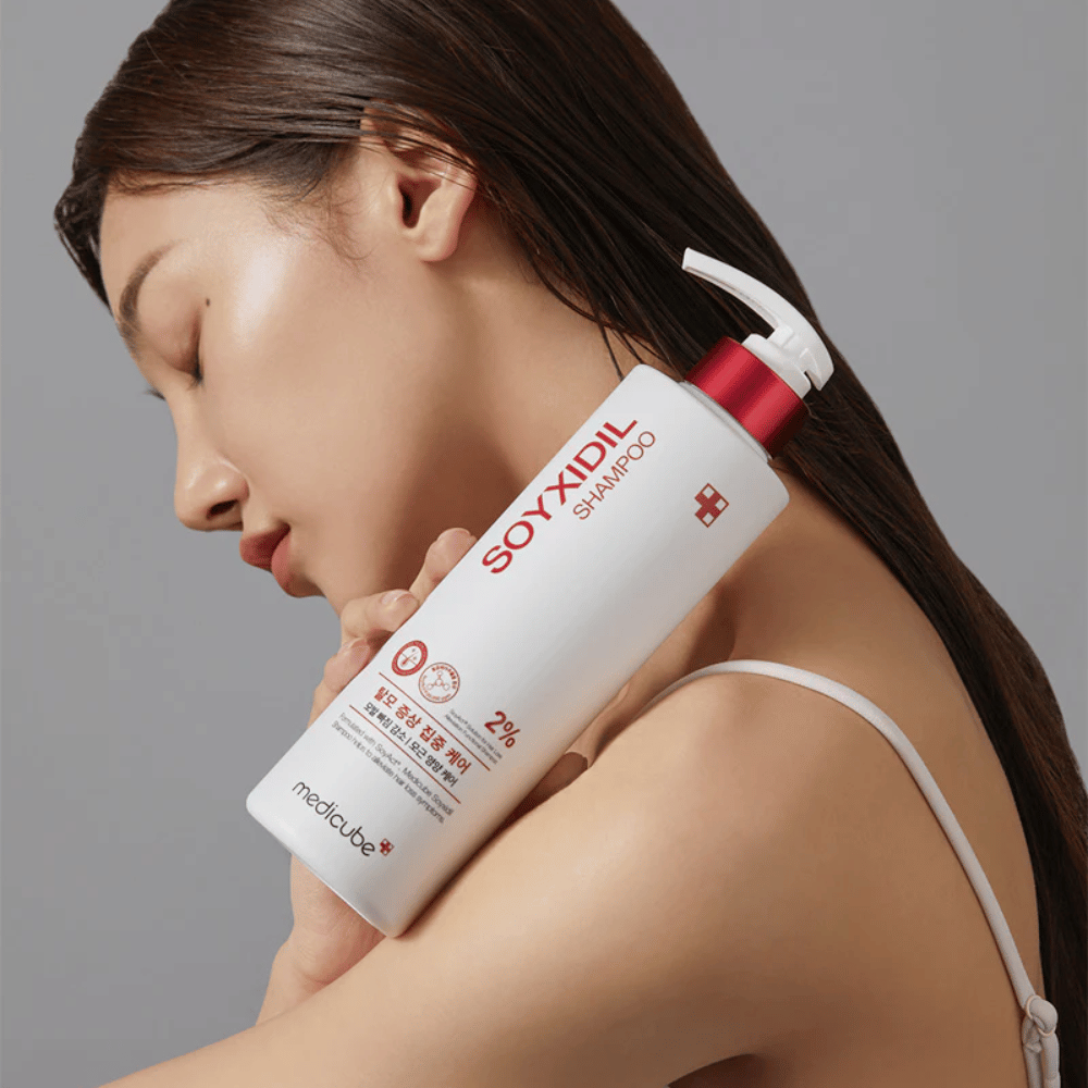 Donna con capelli lunghi appoggia la testa su una bottiglia di Medicube Soyxidil Shampoo, che rinforza il cuoio capelluto e contrasta la caduta dei capelli.