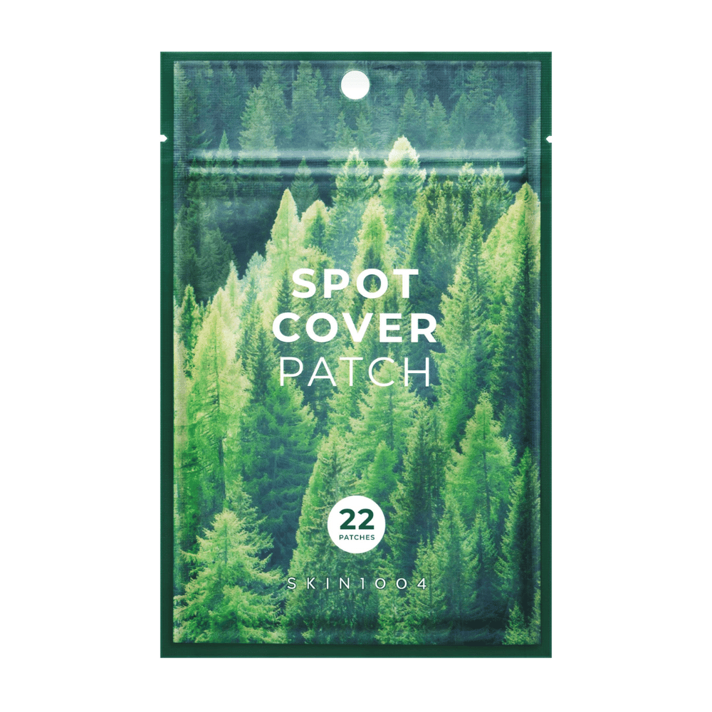 Confezione con "Spot Cover Patch" che contiene 22 cerotti, progettata con un motivo di foresta verde. Il testo "SPOT COVER PATCH" è stampato in bianco sul davanti, e un cerchio indica il numero di cerotti. Il prodotto è del marchio SKIN1004.