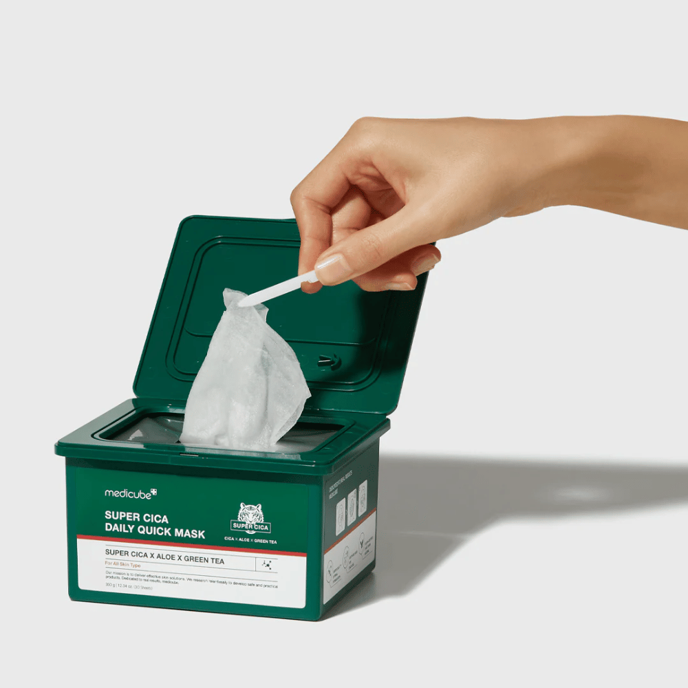 Contenitore verde con coperchio aperto mostra medicube Super Cica Daily Quick Mask. Una mano estrae una maschera in foglio con pinzetta inclusa. Il prodotto contiene Cica, aloe e tè verde, ideale per un'idratazione rapida ed effetto lenitivo.