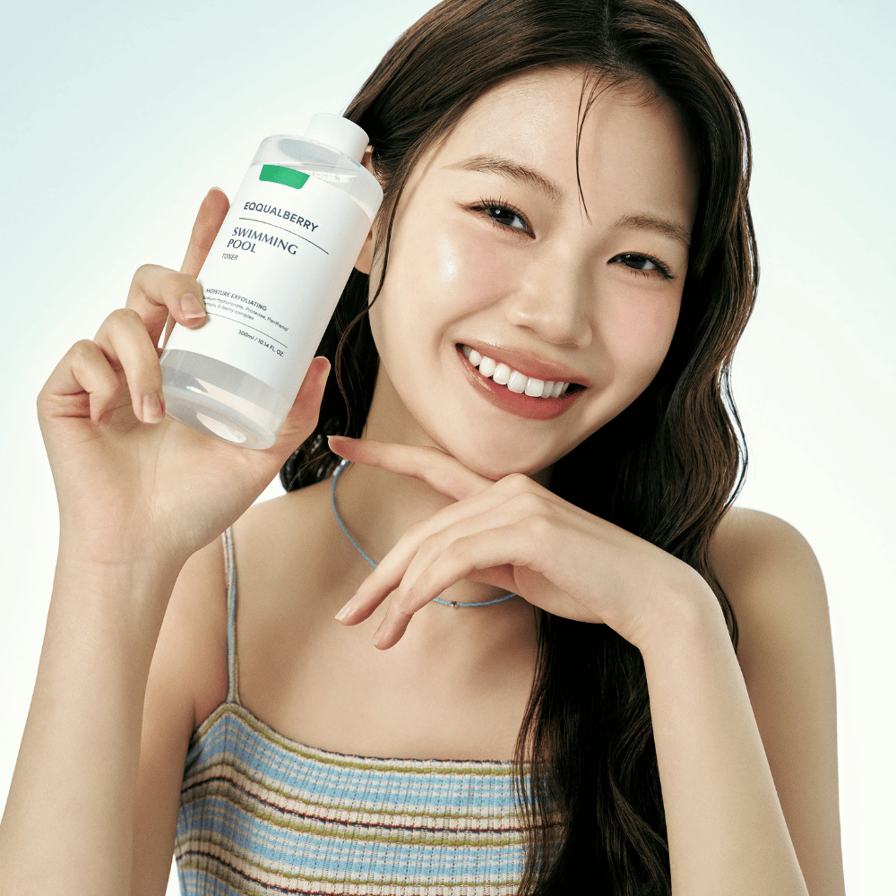 Donna sorridente con pelle radiosa tiene in mano Equalberry Swimming Pool Toner. Look fresco e naturale con trucco leggero e un outfit estivo in blu tonico viso.