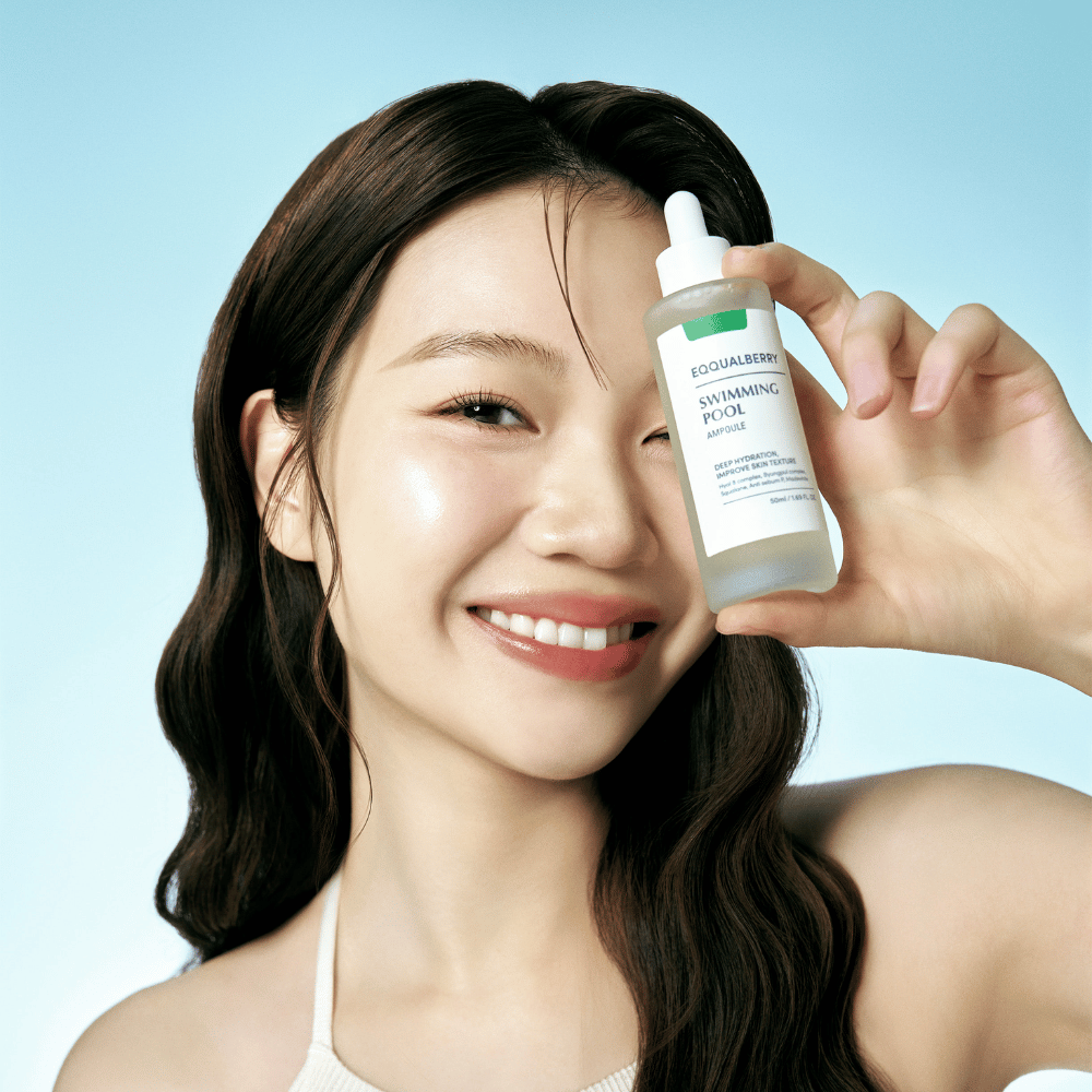 Una donna sorridente tiene in mano Eqqualberry Swimming Pool Ampoule, un prodotto per la cura della pelle per un'idratazione intensa, su uno sfondo azzurro.