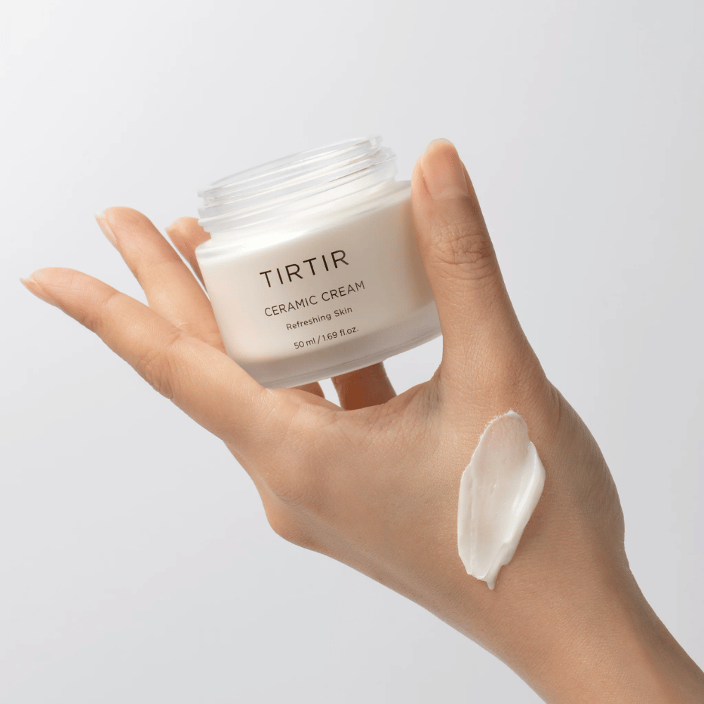 Una mano tiene un barattolo con TIRTIR Ceramic Cream. Sul dorso della mano è stata applicata una quantità di crema. La crema sembra essere densa e idratante. La confezione indica che il contenuto è per "Refreshing Skin" e la quantità è di 50 ml / 1.69 fl oz.