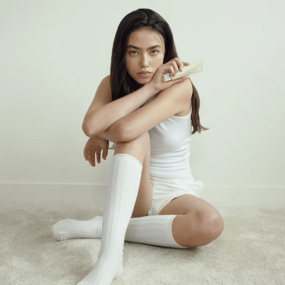 Immagine lifestyle con una modella che tiene il prodotto in un ambiente luminoso e minimalista. L’immagine trasmette una sensazione di skincare pulita, naturale e calma, collegata al glow e all’effetto brightening.